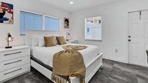 Une chambre à coucher avec un lit, des tables de chevet, une fenêtre et une porte.