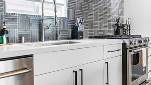 A modern kitchen with a stainless steel range hood, a double sink, and a tiled backsplash.