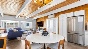 A modern kitchen with a large stainless steel refrigerator, wooden ceiling beams, and a dining area with a round table and chairs.