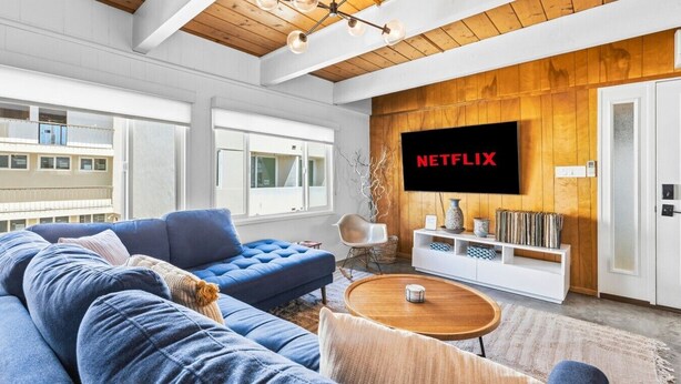 A modern living room with a blue sofa, a wooden coffee table, and a mounted TV displaying 'NETFLIX'.