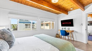 A bedroom with a bed, a desk, a chair, a TV mounted on the wall, and a window.