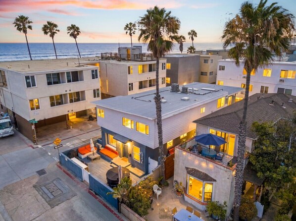 A multi-story residential building with a rooftop deck, a covered outdoor seating area, and a view of the ocean.