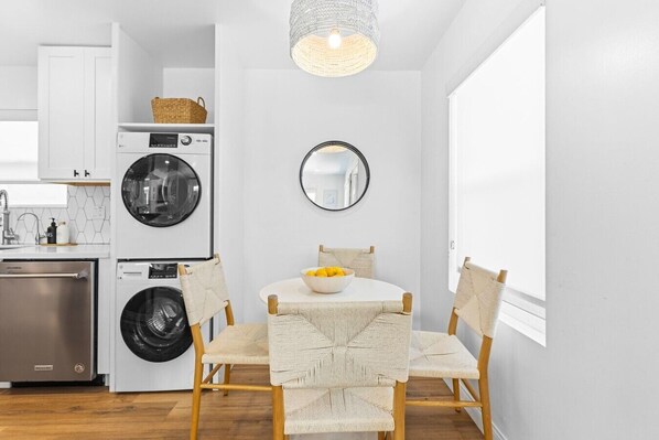 A compact kitchen with a washing machine, a sink, and a dining area with a round table and chairs.