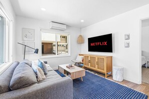 A modern living room with a grey sofa, a wooden cabinet, a coffee table, and a large TV screen displaying 'NETFLIX'.