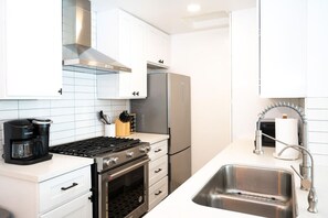 Uma cozinha moderna com armários brancos, fogão de aço inoxidável, forno embutido, máquina de café e pia com torneira.