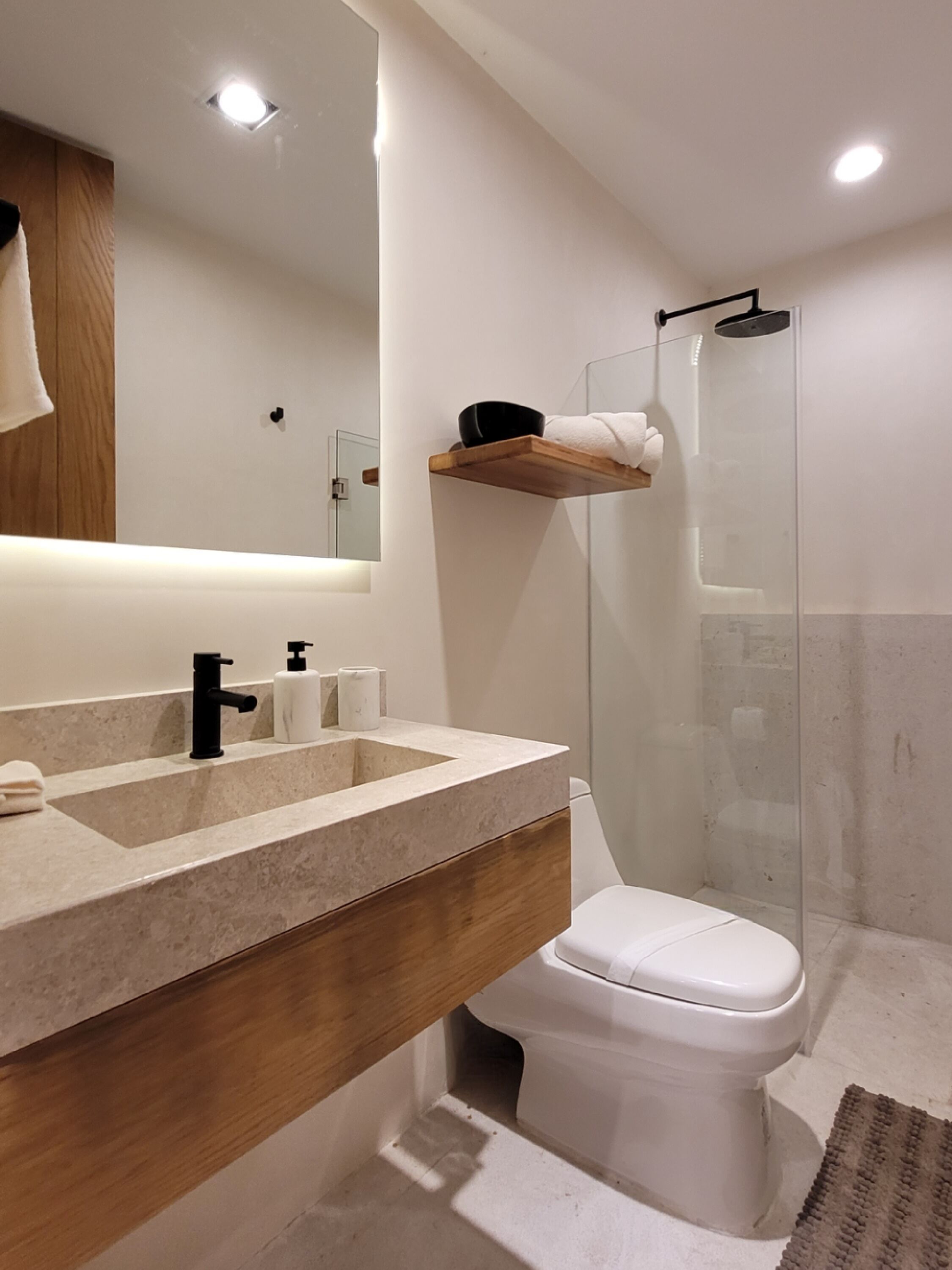 A modern bathroom with a large mirror, a sink with a wooden vanity, a toilet, and a glass-enclosed shower.