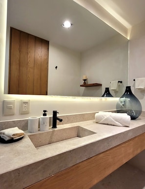 A modern bathroom with a large mirror, a wooden cabinet, a sink with a black faucet, and two vases on the counter.
