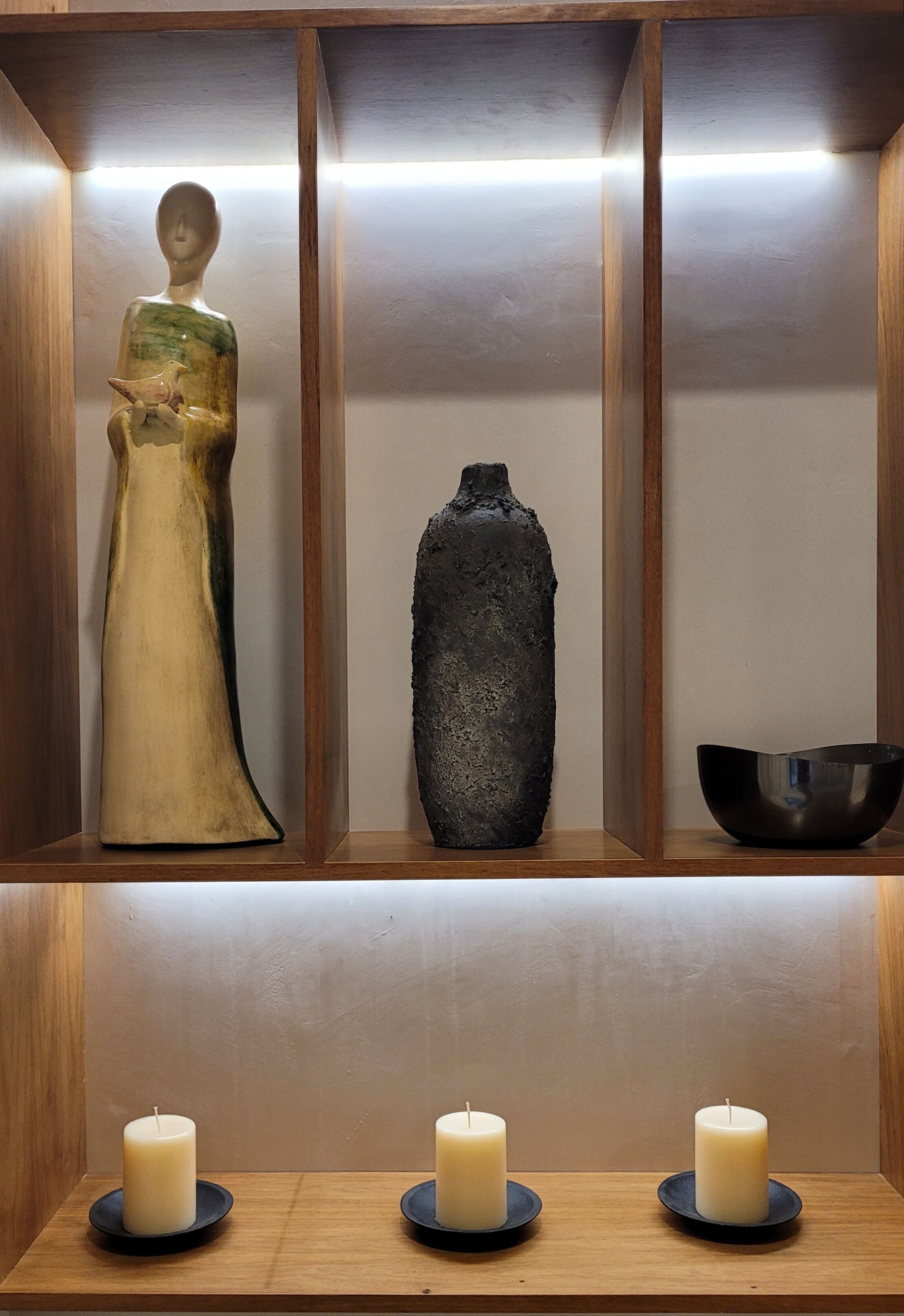 A wooden shelf with a ceramic figure, a textured vase, and a black bowl.
