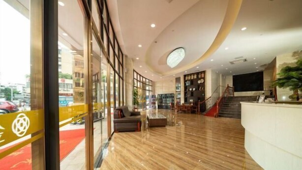 A modern hotel lobby with a curved reception desk, a staircase, and a seating area with a red carpet. - Jinchi Business Hotel (Jiangmen)