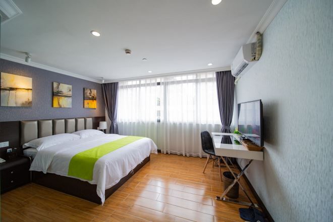A hotel room with a bed, desk, and chair, a television, and artwork on the wall.