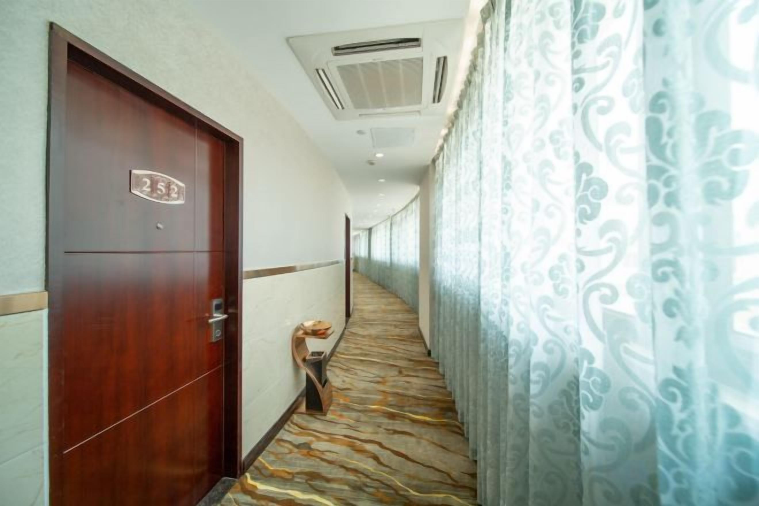 Ein Hotelgang mit einer Holztür mit der Aufschrift '255', einem gemusterten Teppich und einer Wand mit einem dekorativen Vorhang.