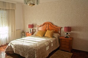 A bedroom with a patterned bedspread, two bedside lamps, and a wooden headboard. - Apartment in a house with garden, pool and barbecue, 10 minutes from Pontevedra (Vilaboa, Pontevedra)