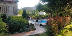 A pool area with a patio, surrounded by lush greenery and a stone building. - Apartment in a house with garden, pool and barbecue, 10 minutes from Pontevedra (Vilaboa, Pontevedra)