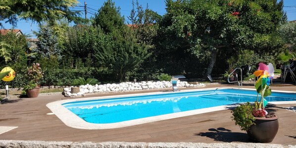 A swimming pool with a stone border, surrounded by trees and a stone wall. - Apartment in a house with garden, pool and barbecue, 10 minutes from Pontevedra (Vilaboa, Pontevedra)