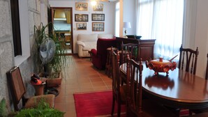 A dining area with a wooden table and chairs, a red rug, and a fan. There are potted plants and a red chair. - Barranqueiro House (Vilaboa, Pontevedra)