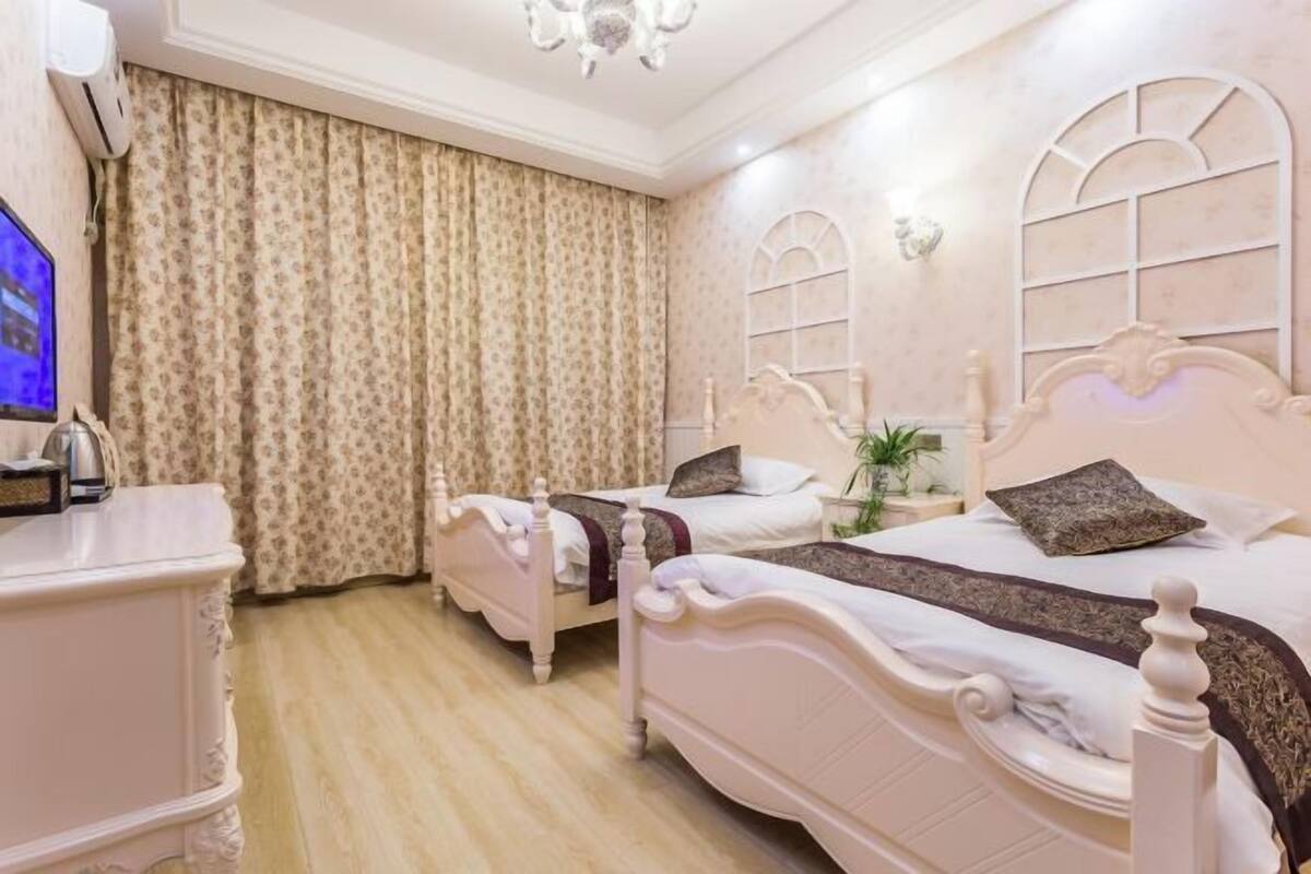 A hotel room with two beds, a TV, a dresser, and a chandelier.