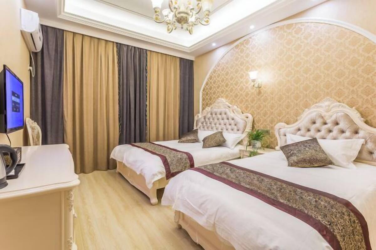 A hotel room with two beds, a desk with a computer, a TV, and a chandelier.