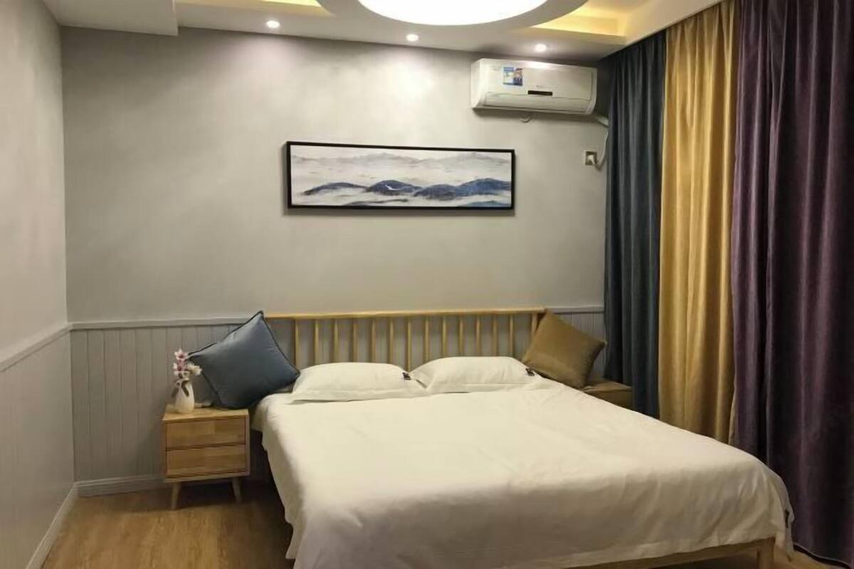 A bedroom with a bed, bedside tables, a wall-mounted air conditioner, and a framed picture.