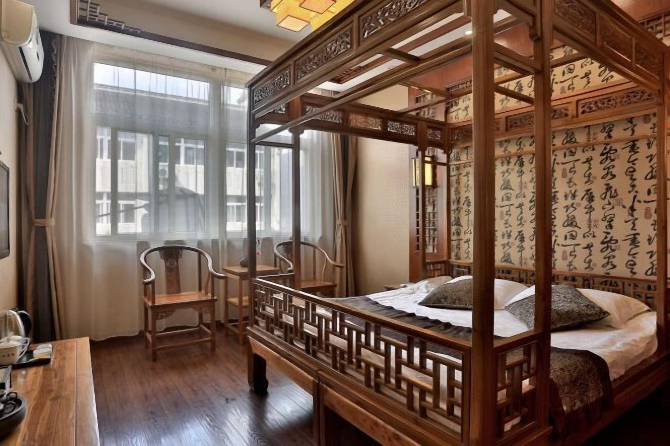 Una cama tradicional con dosel de madera y cuatro columnas, un escritorio con silla, y una ventana con cortinas.