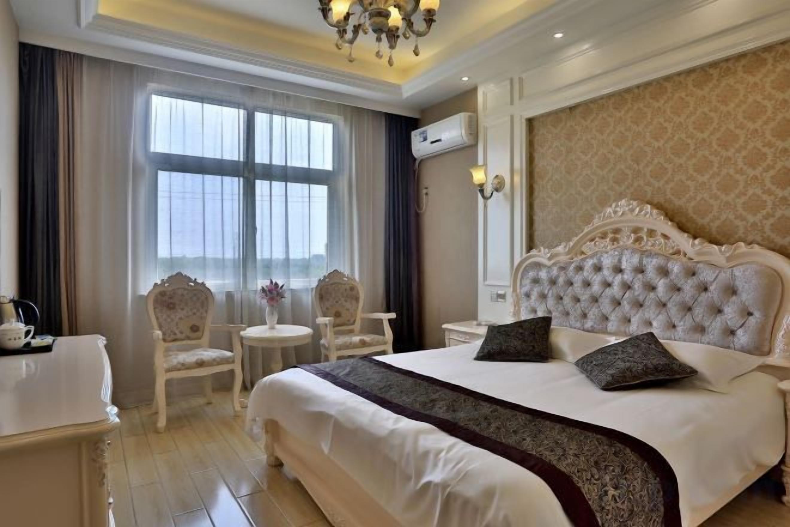 A hotel room with a large bed, two chairs, a small table, and a window with curtains.