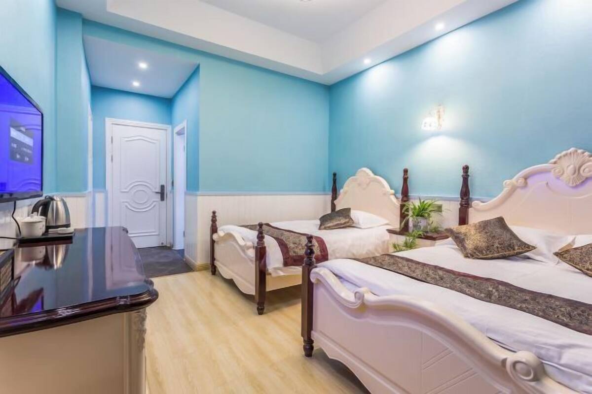 A hotel room with two beds, a wooden desk, a television, and a door.