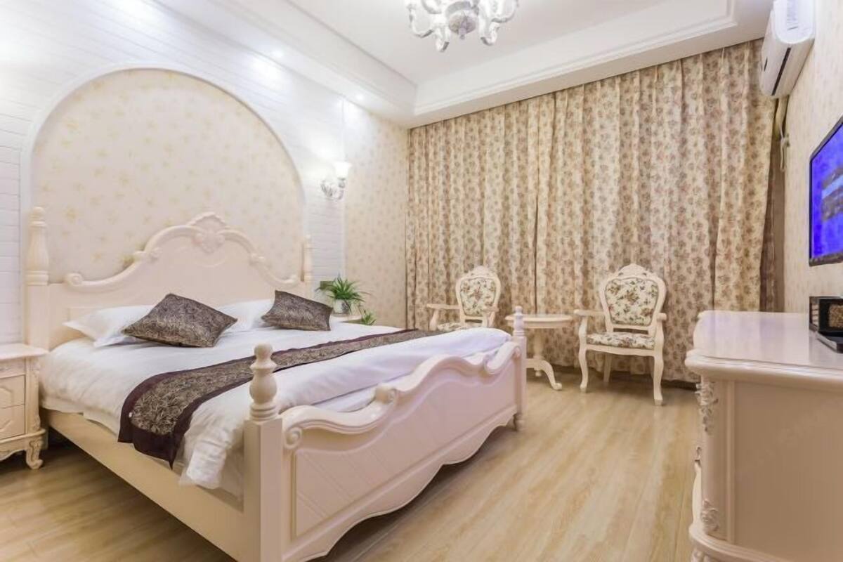 A bedroom with a bed, two chairs, a small table, and a TV.