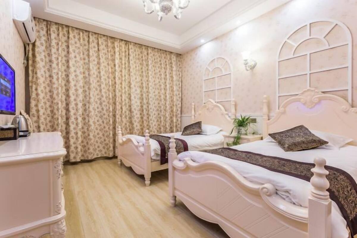 A hotel room with two beds, a TV, a dresser, and a chandelier.