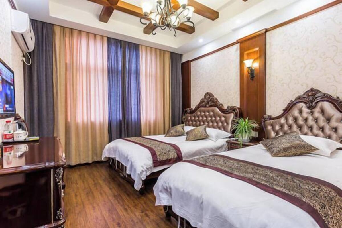 A hotel room with two beds, a wooden desk, a television, and a chandelier.