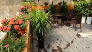 A wooden deck with potted plants and flowers, a round table, and two chairs.