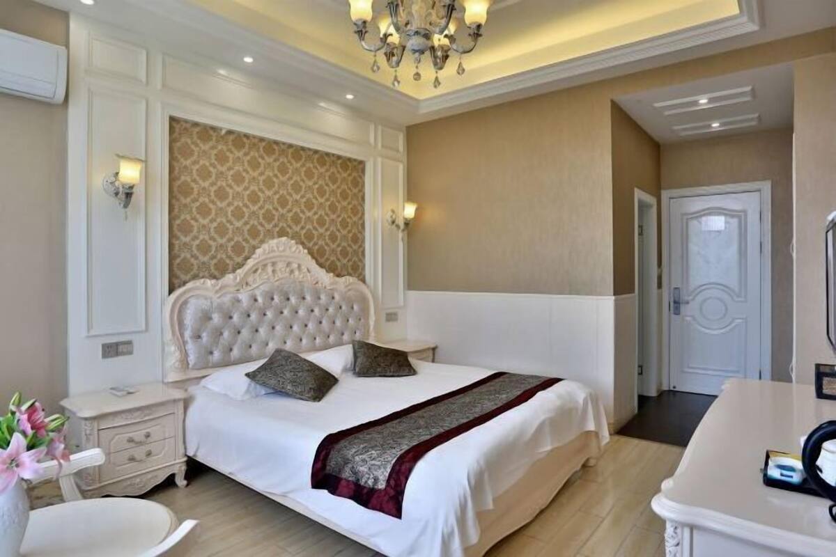 A bedroom with a large bed, a nightstand, a bedside table, a chair, and a desk with a chair.