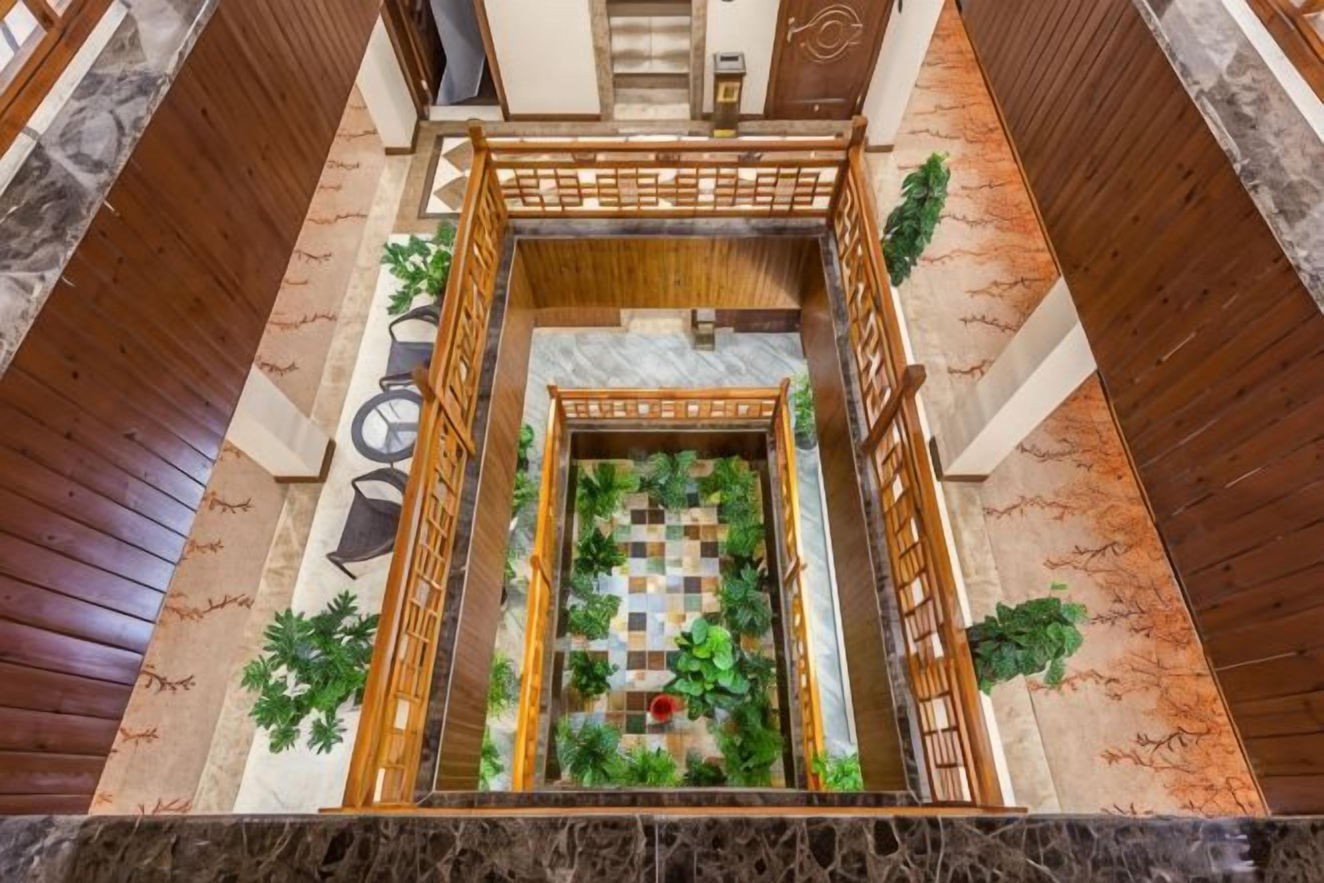 Un vestíbulo de hotel con un jardín central, barandales de madera y suelo de mármol.