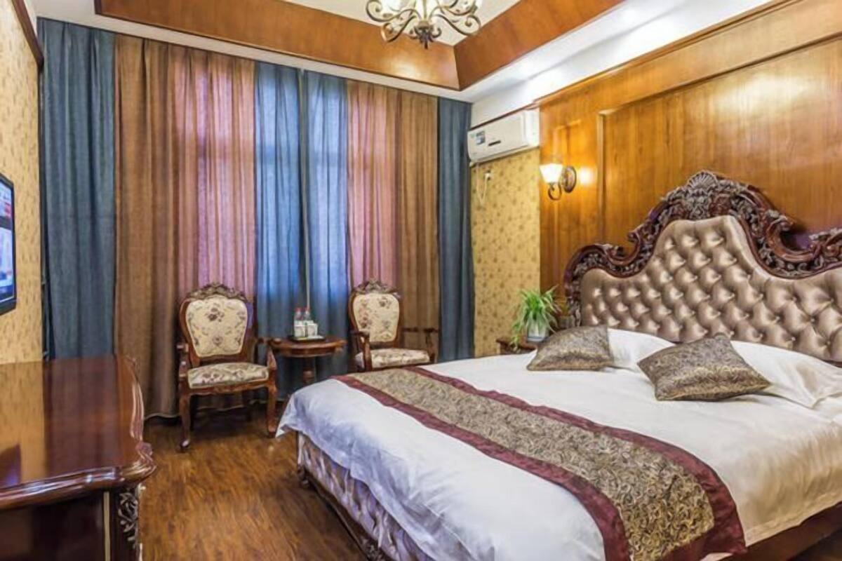 A bedroom with a large bed, two chairs, a small table, and an air conditioning unit.