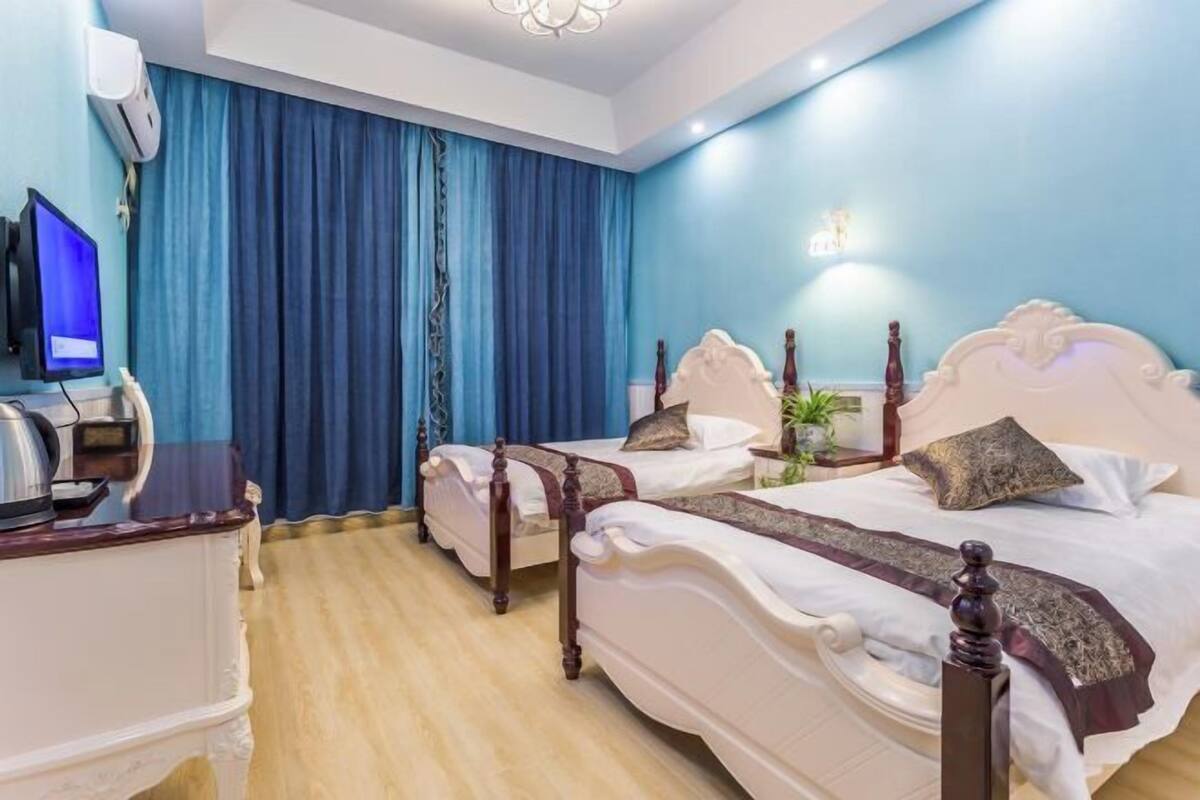 A hotel room with two beds, a television, a desk, and a large window with curtains.