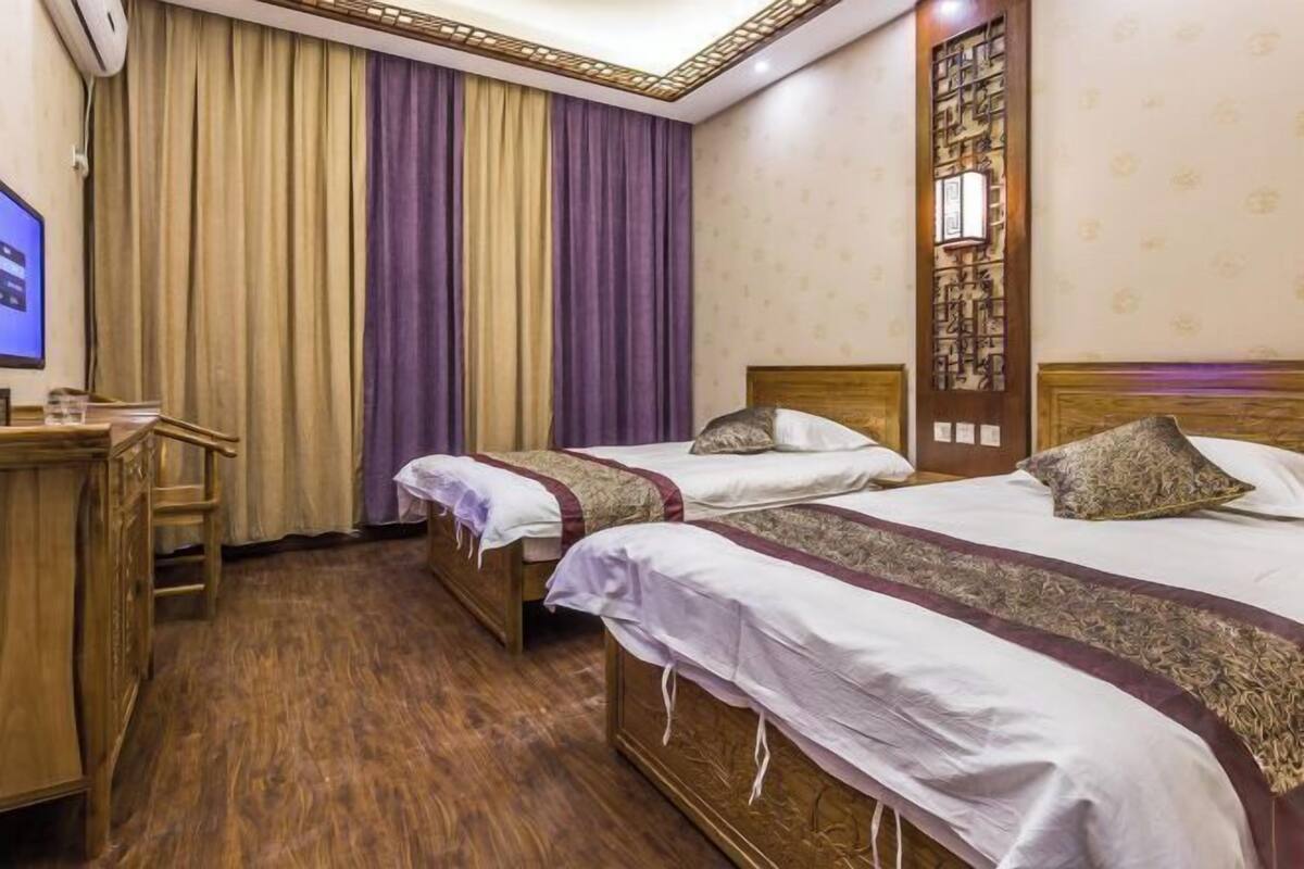 A hotel room with two single beds, a wooden desk, a television, and a large window with curtains.