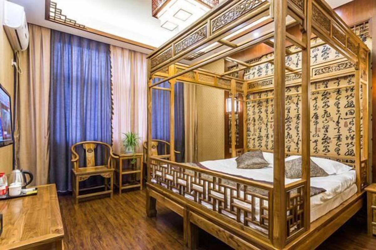 A traditional wooden four-poster bed with a pillow, a wooden desk with a chair, and a television.