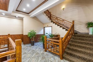 Un vestíbulo de hotel con escalera de madera, suelo de mármol y plantas en macetas.