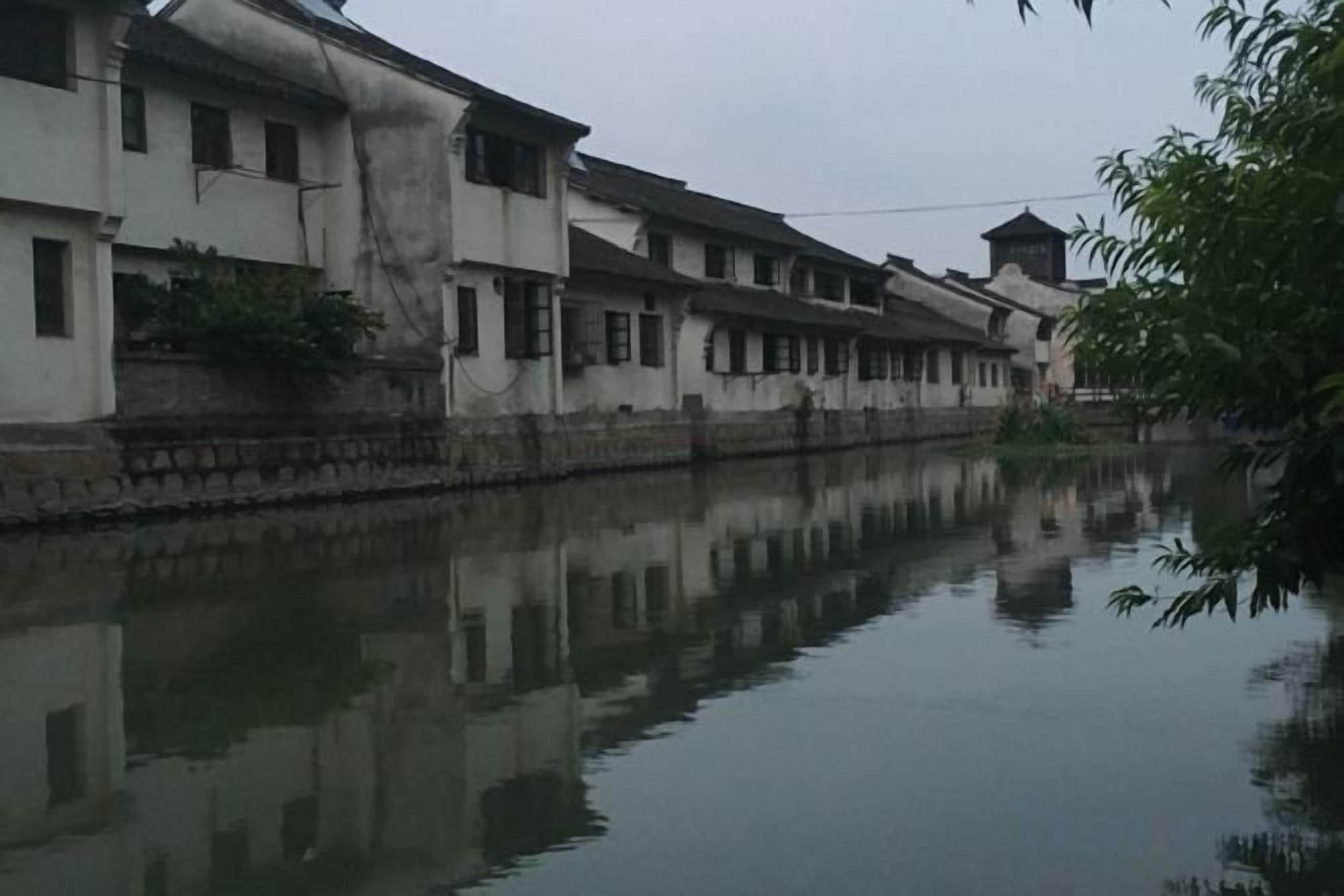 Una hilera de edificios tradicionales a lo largo de un río tranquilo, con reflejos visibles en la superficie del agua.