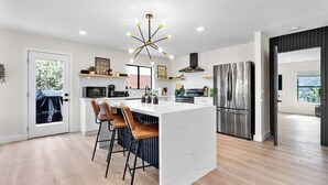 Una cocina moderna con una isla central, taburetes de bar, un refrigerador de acero inoxidable y una lámpara colgante.