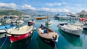 A marina with various boats docked, calm water, and a mountainous backdrop. - Sea Glass Sunset (Rafailovići)