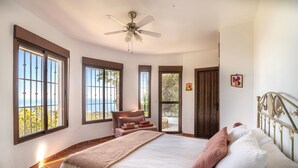 A bedroom with a large bed, a ceiling fan, and multiple windows offering a view of the outdoors. - Los Naranjos - Luxury villa with private pool and stunning sea view (Sayalonga)