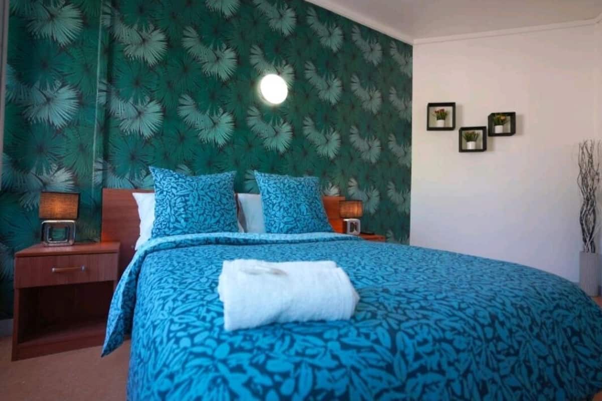 A hotel room with a large bed, a nightstand, a wall clock, and three framed pictures on the wall.