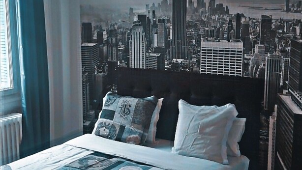 Un dormitorio con una cama grande, un mural de paisaje urbano en la pared y una ventana con cortinas.