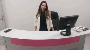 Un mostrador de recepción con un monitor de computadora, un teléfono y algunos folletos.