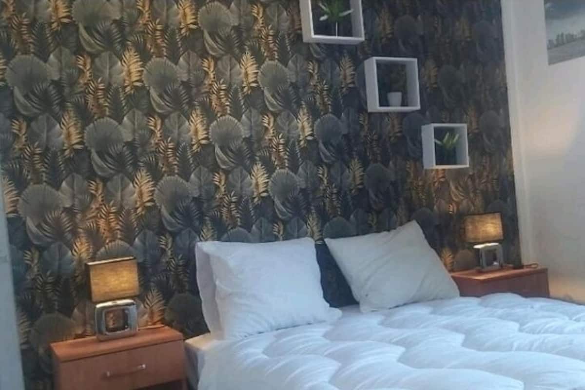 A bedroom with a bed, two bedside tables, and a wall with a leaf-patterned wallpaper.