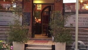 Entrada de restaurante con terraza, fachada de ladrillo y señalización en un idioma extranjero.