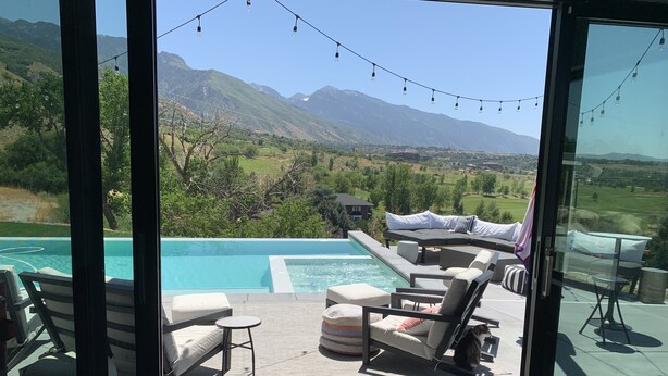 Ein Poolbereich mit Liegestühlen, einem kleinen Tisch und Blick auf Berge sowie einen Golfplatz.