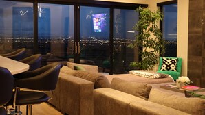 Ein modernes Wohnzimmer mit Blick auf die Stadt, bequemen Sitzgelegenheiten und einem großen Fenster.