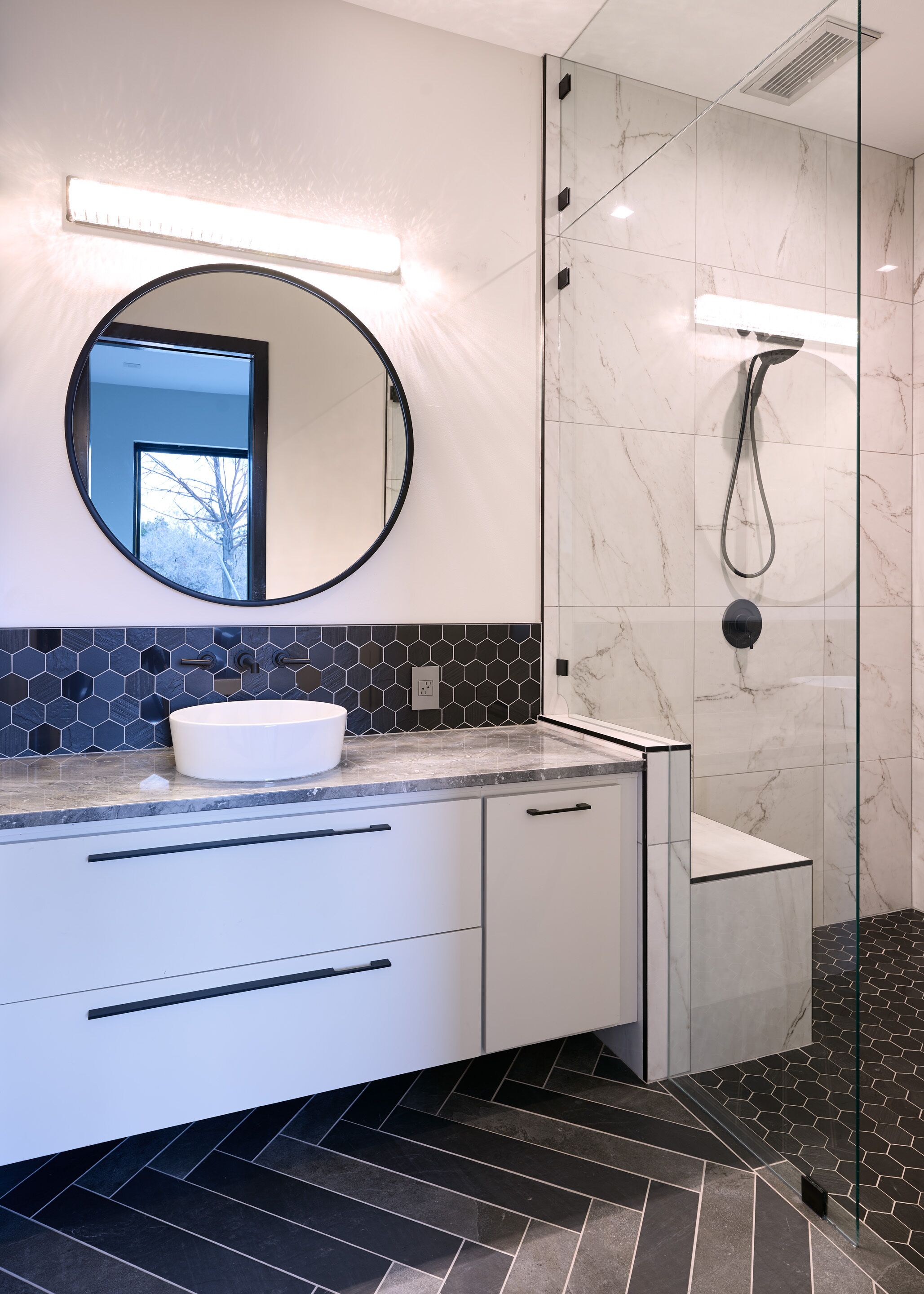 A modern bathroom with a round mirror, a white sink, and a glass-enclosed shower.