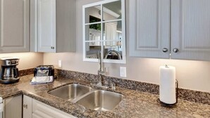 A kitchen with granite countertops, stainless steel sinks, a coffee maker, and a mirror above the sink.