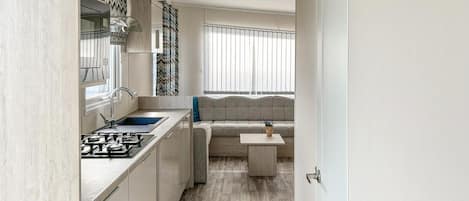 A compact kitchen with a gas stove, sink, and modern cabinetry. A cozy seating area with a patterned sofa and a small table is visible in the background.